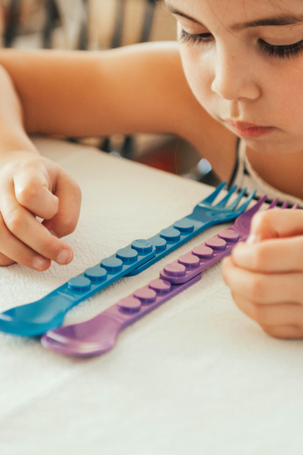 Child stacking blue and purple utensil handles into a long chain
