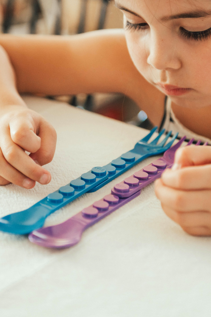 Child stacking blue and purple utensil handles into a long chain