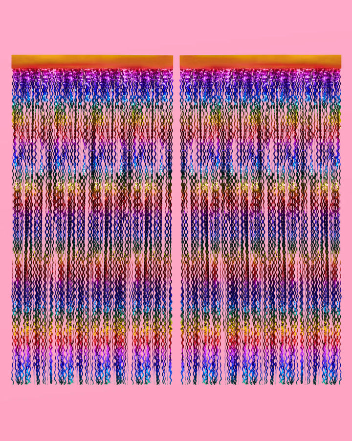 Two rainbow wavy foil curtain panels hung side by side on a pink wall