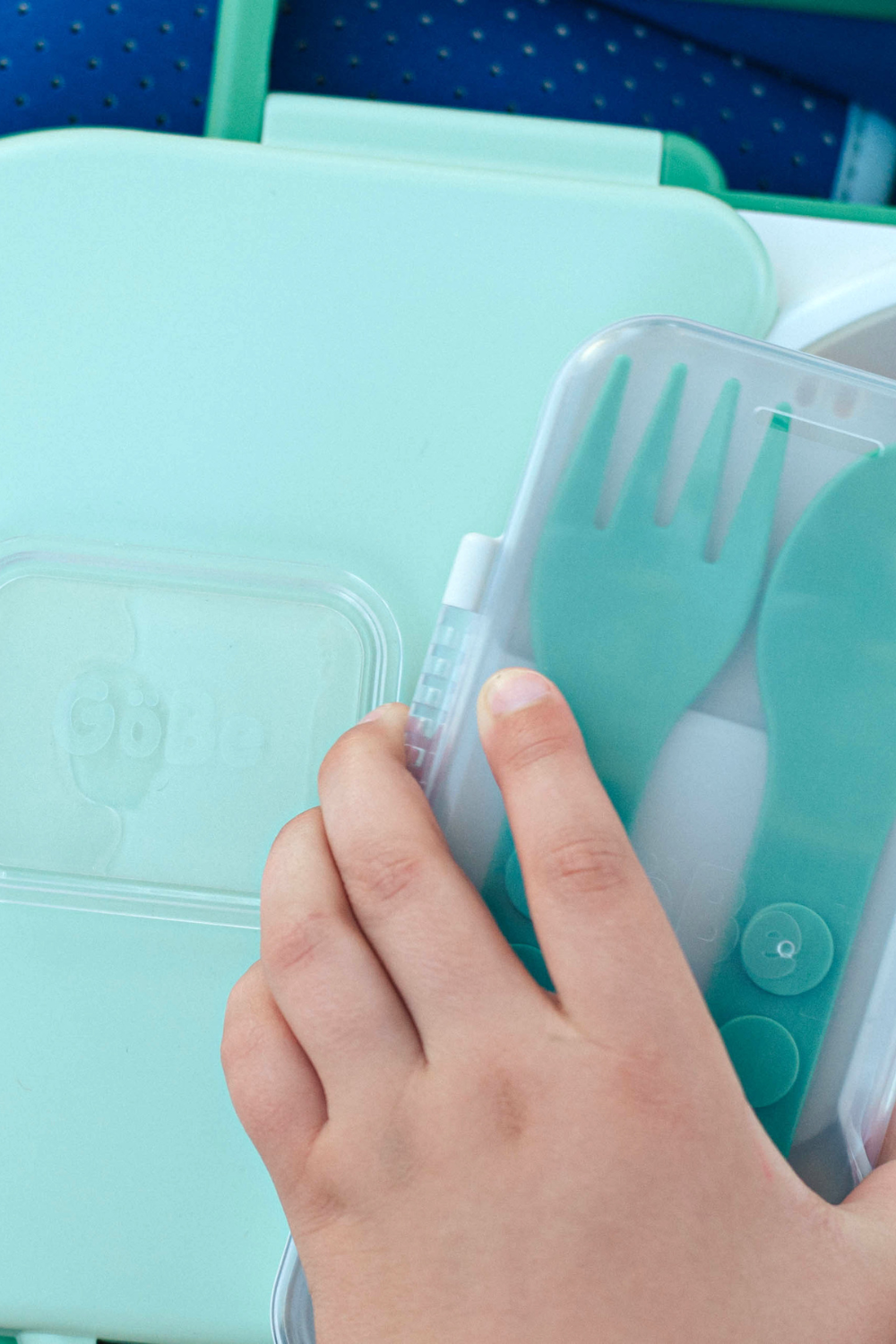 Child sliding the utensil travel case out of a mint lunchbox lid