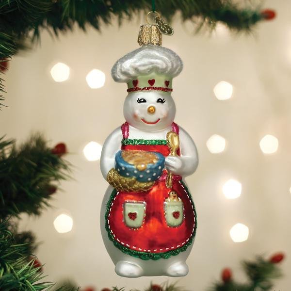 Snow woman chef glass ornament with a mixing bowl hanging on a lit Christmas tree