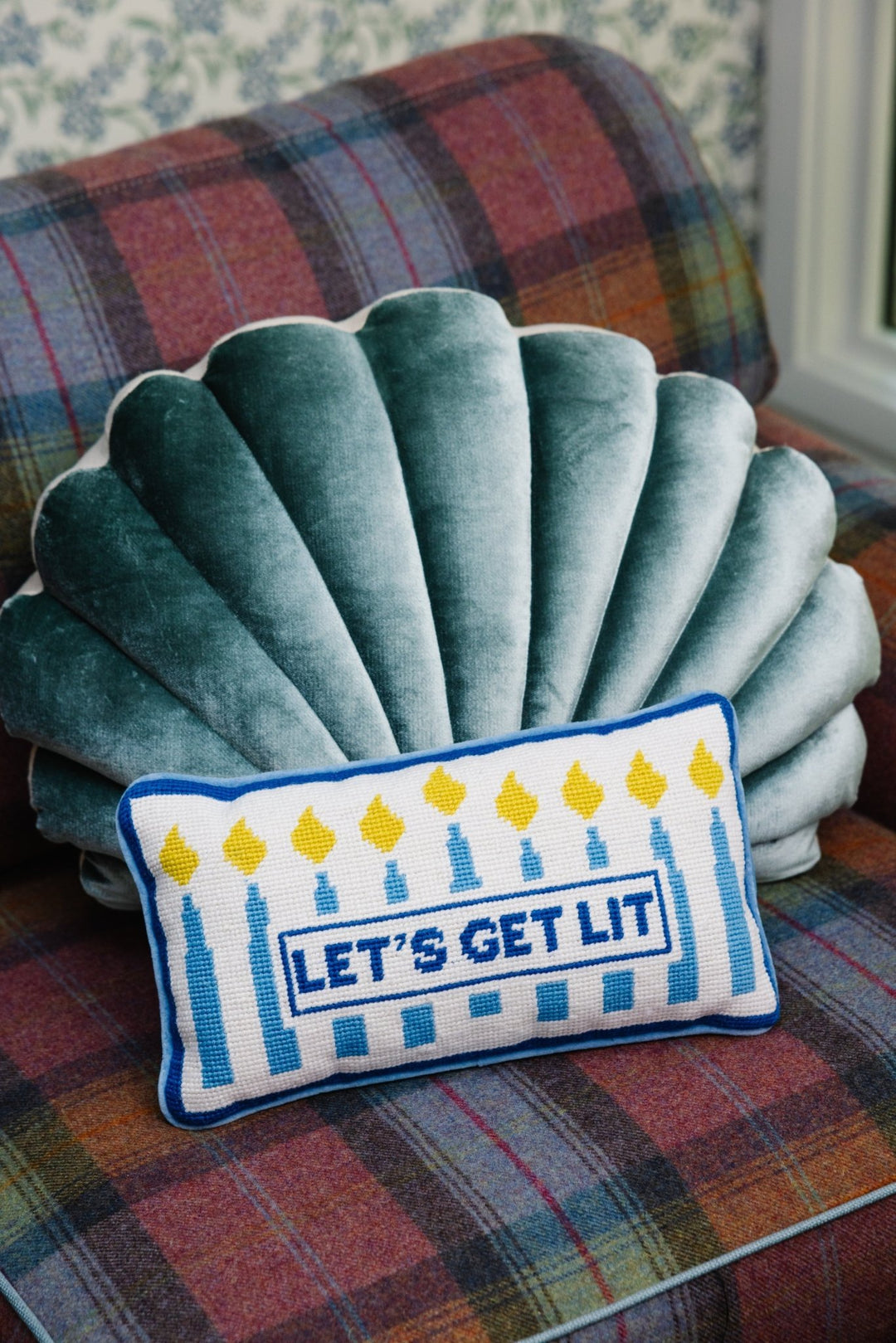 Let's Get Lit Hanukkah needlepoint pillow with menorah candles styled with a green velvet shell pillow on a plaid chair