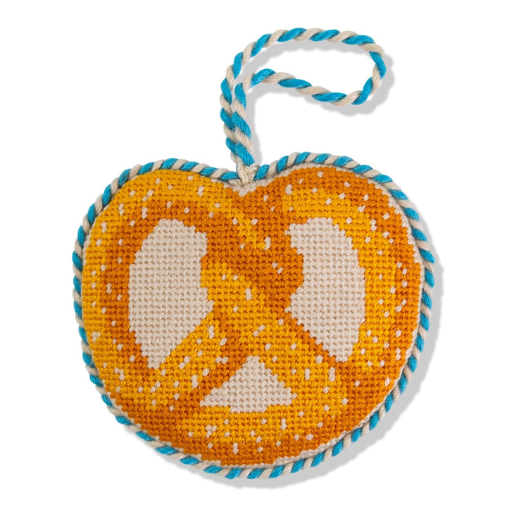 Pretzel needlepoint ornament, front view of a golden pretzel on cream with a teal and white cord