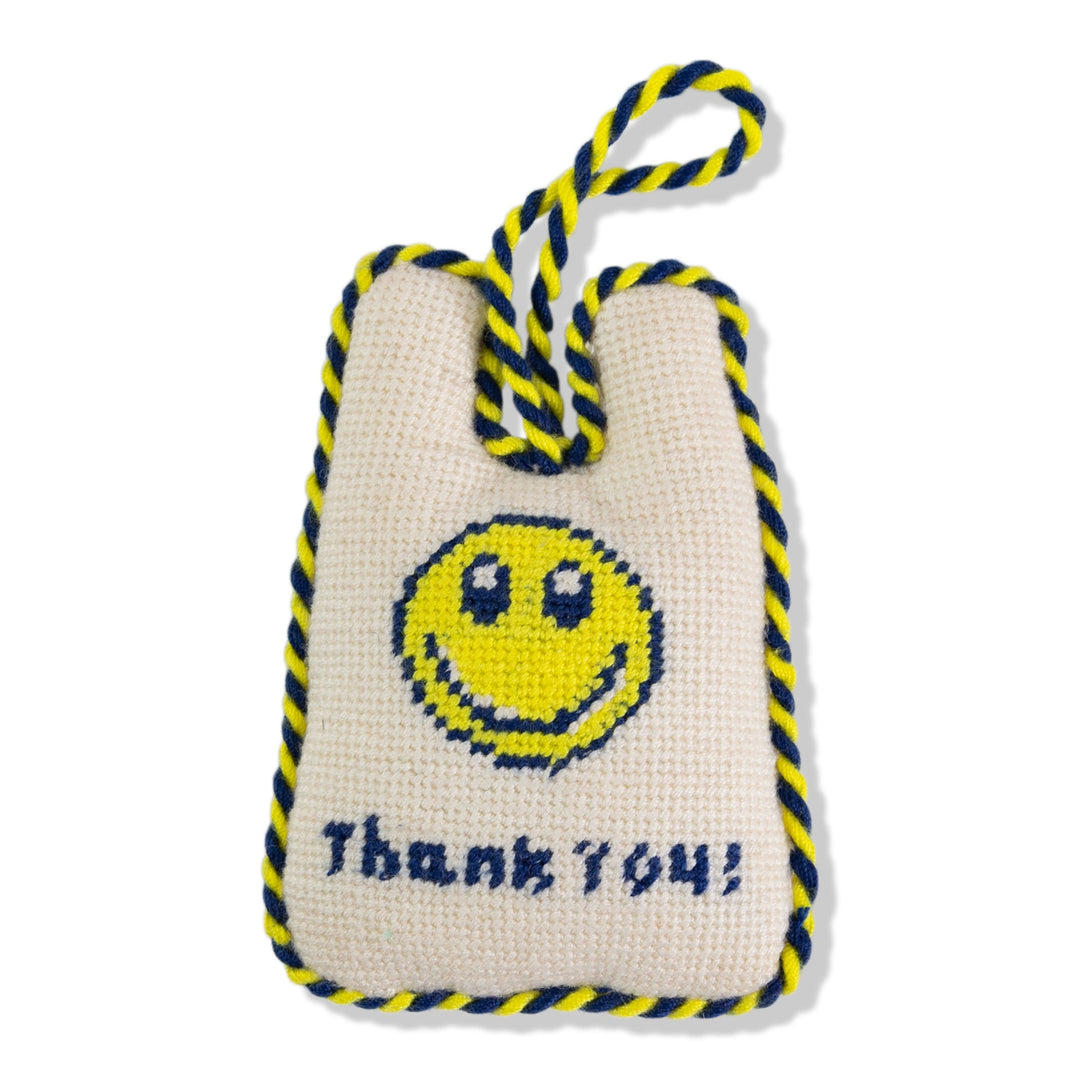 Takeout bag needlepoint ornament with a yellow smiley face and Thank You lettering, front view on white