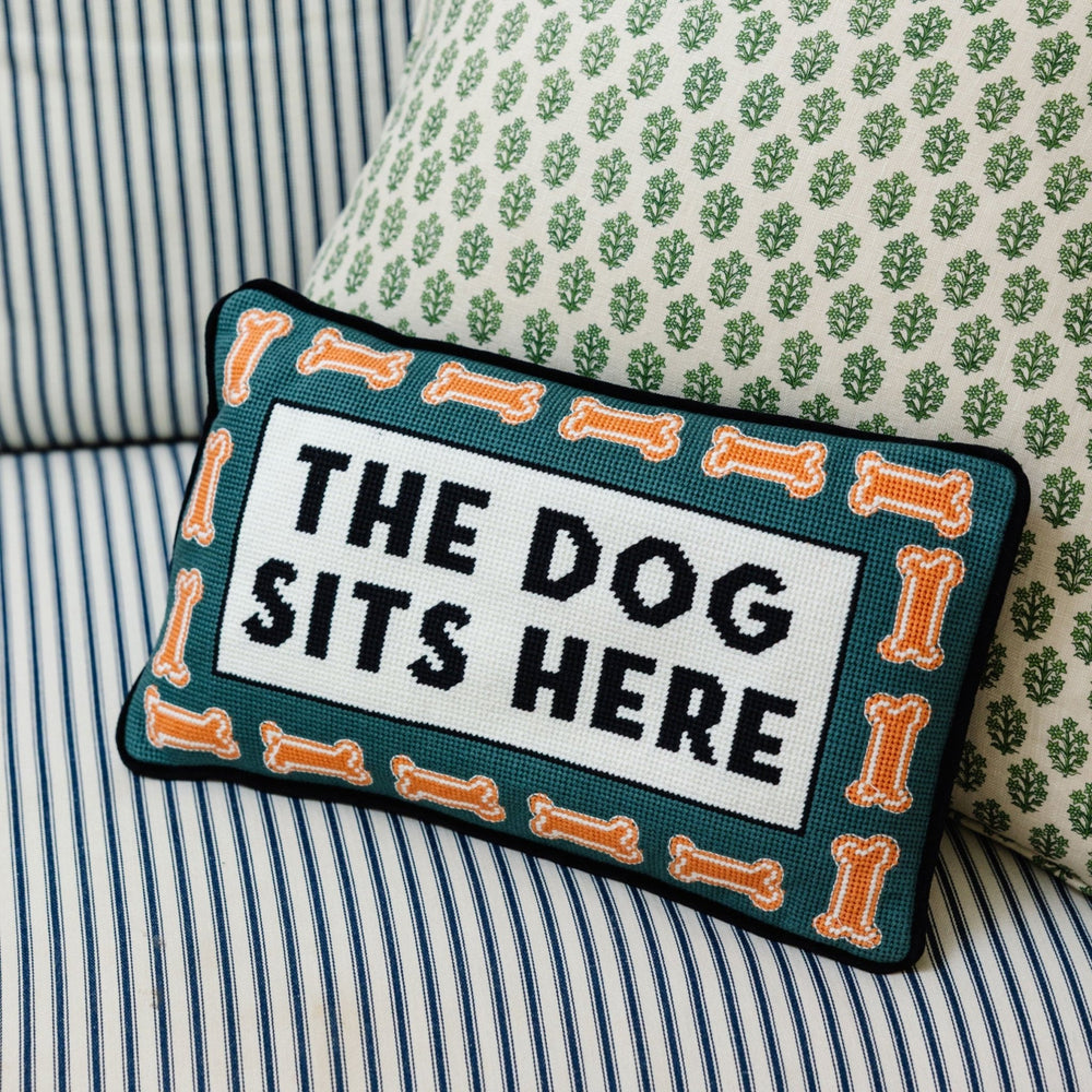 The Dog Sits Here needlepoint pillow with a dog bone border styled on striped and green floral pillows