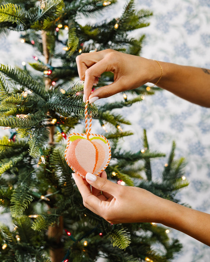 Two hands hanging the peach needlepoint ornament on a Christmas tree