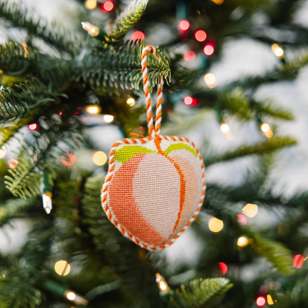 Peach ornament hanging on a green Christmas tree branch with soft lights