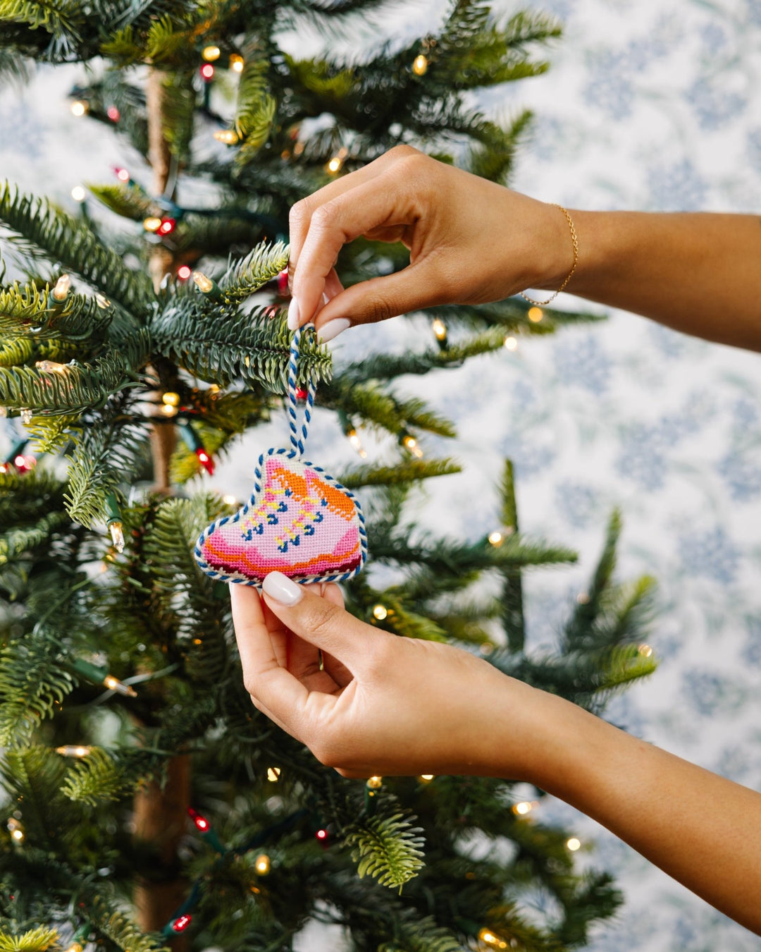 Two hands placing the pink snow boots needlepoint ornament on a Christmas tree
