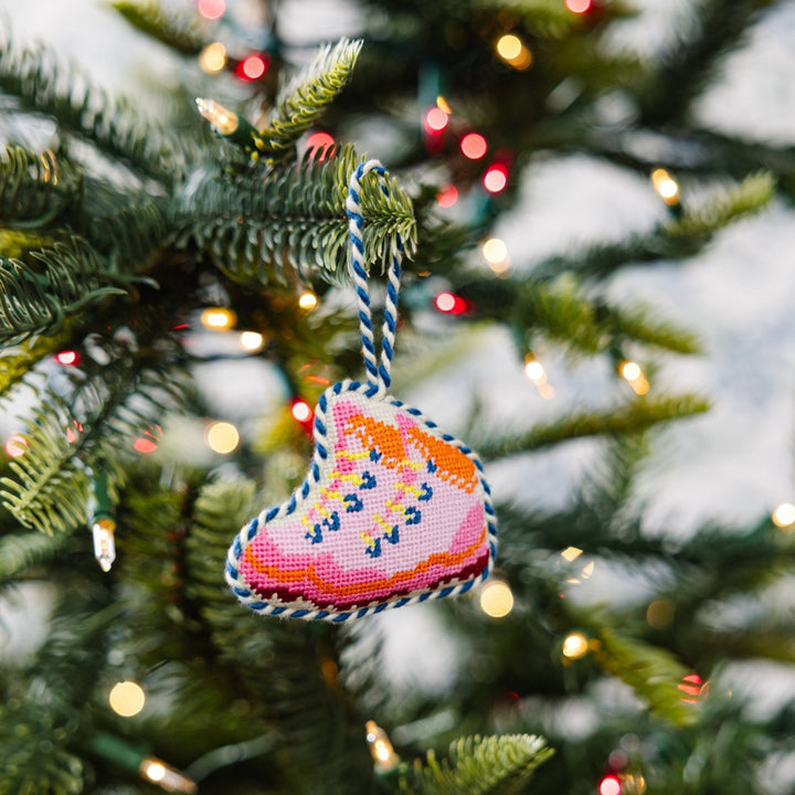 Snow boots ornament hanging on a green Christmas tree branch with blurred lights