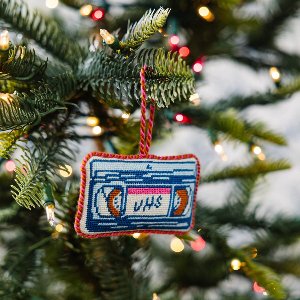 VHS tape ornament hanging from a Christmas tree branch with warm lights behind it