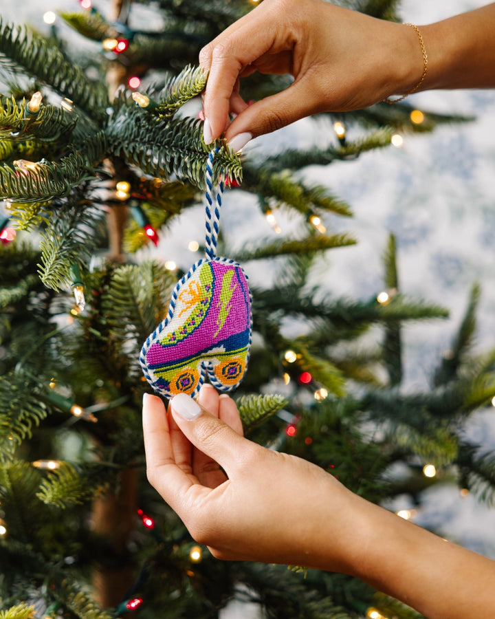 Two hands hanging the magenta roller skate needlepoint ornament on a Christmas tree