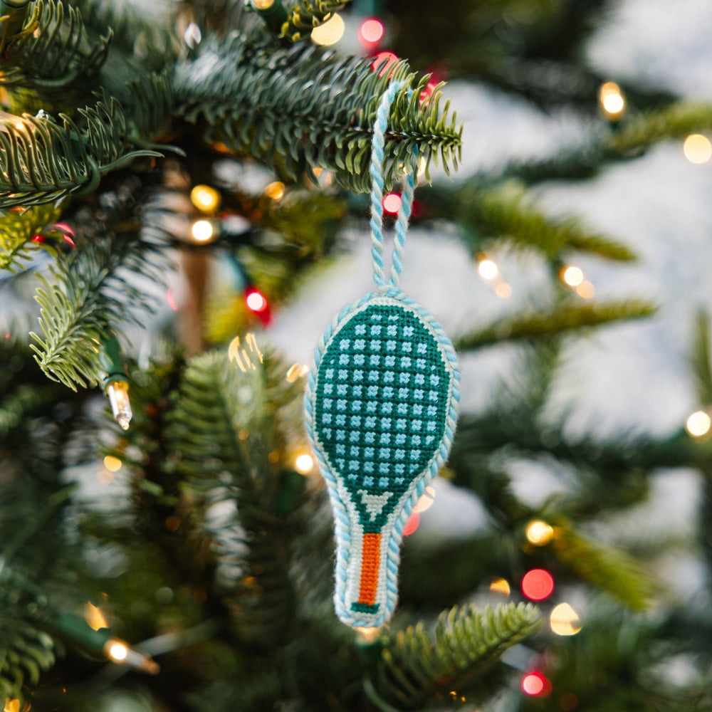 Green tennis racket ornament hanging on a Christmas tree branch among soft white lights