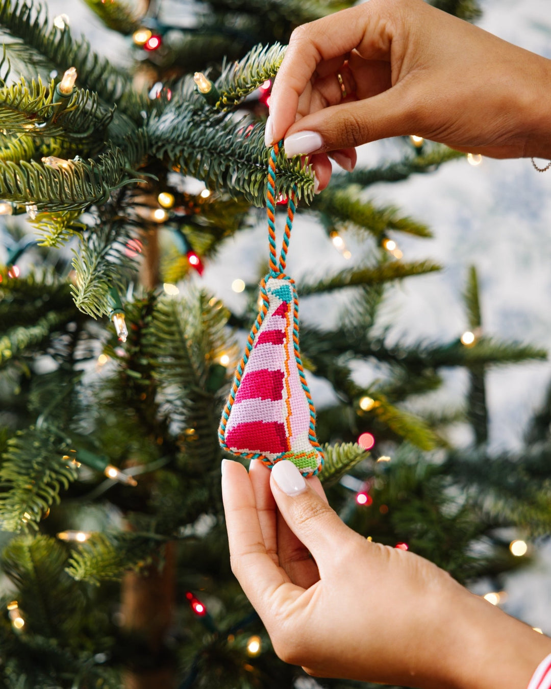 Two hands hanging the sailboat needlepoint ornament on a Christmas tree