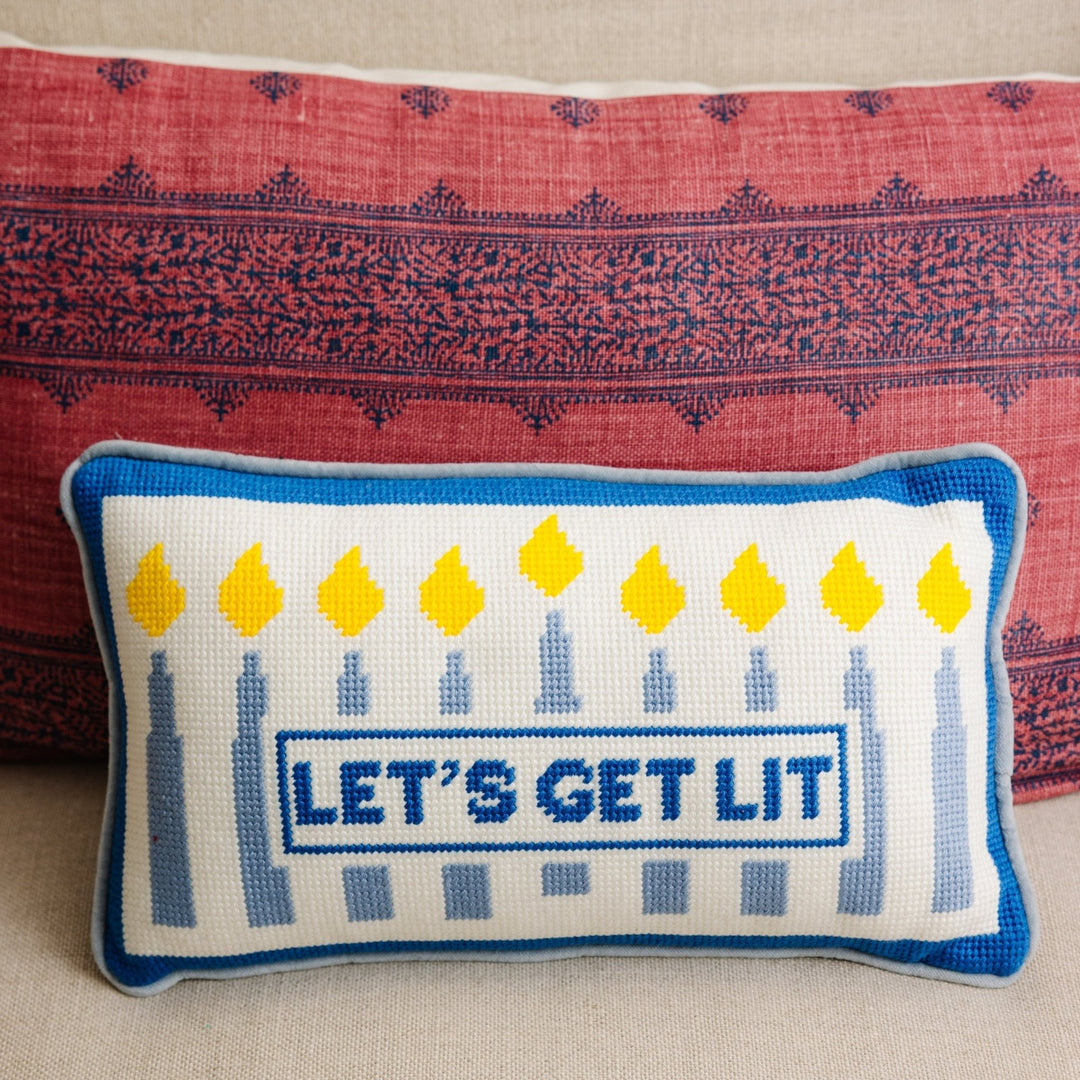 Let's Get Lit Hanukkah menorah needlepoint pillow styled against a red patterned pillow for holiday home decor