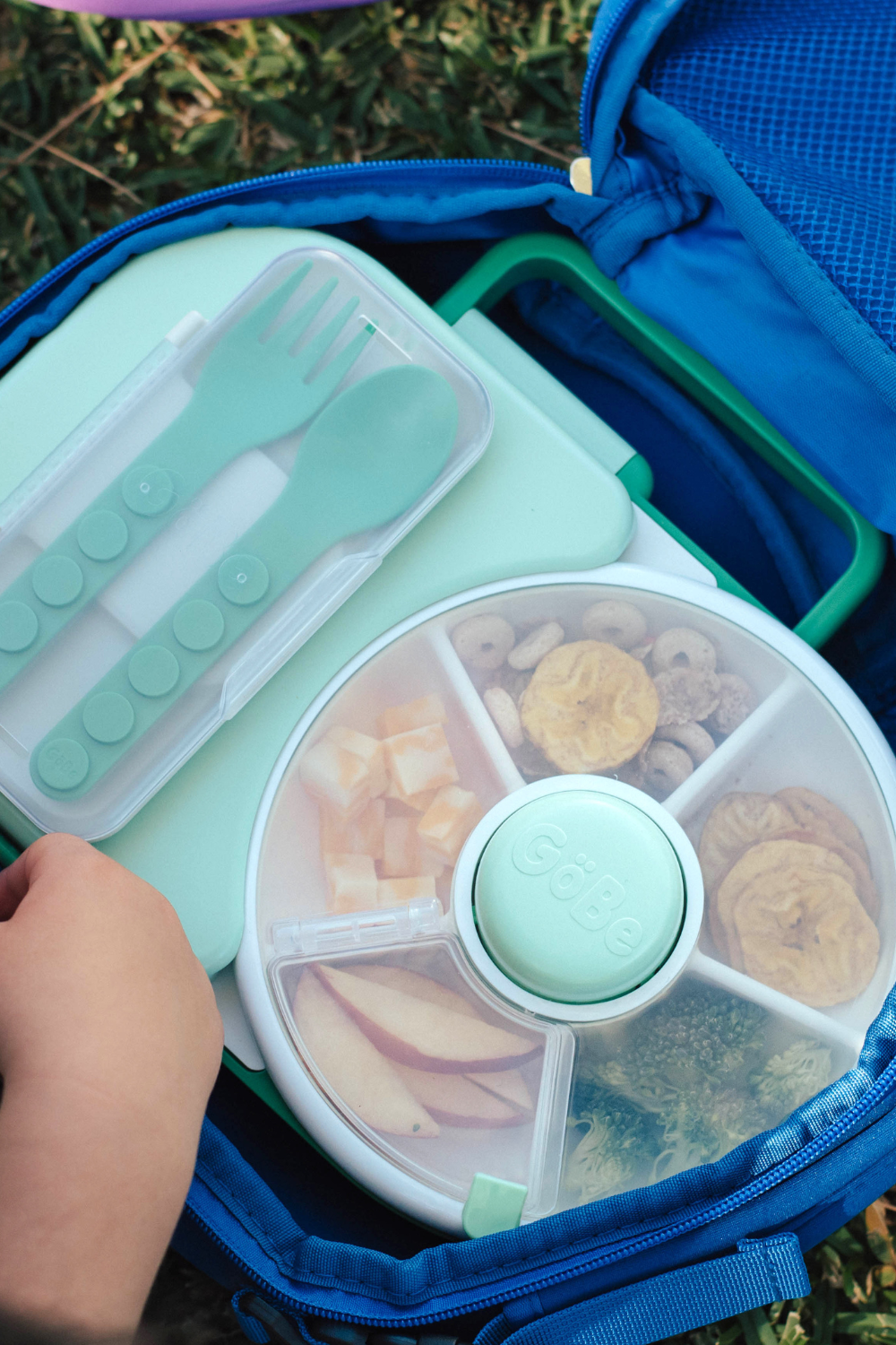Green fork and spoon in their case tucked into a lunchbox beside a snack spinner