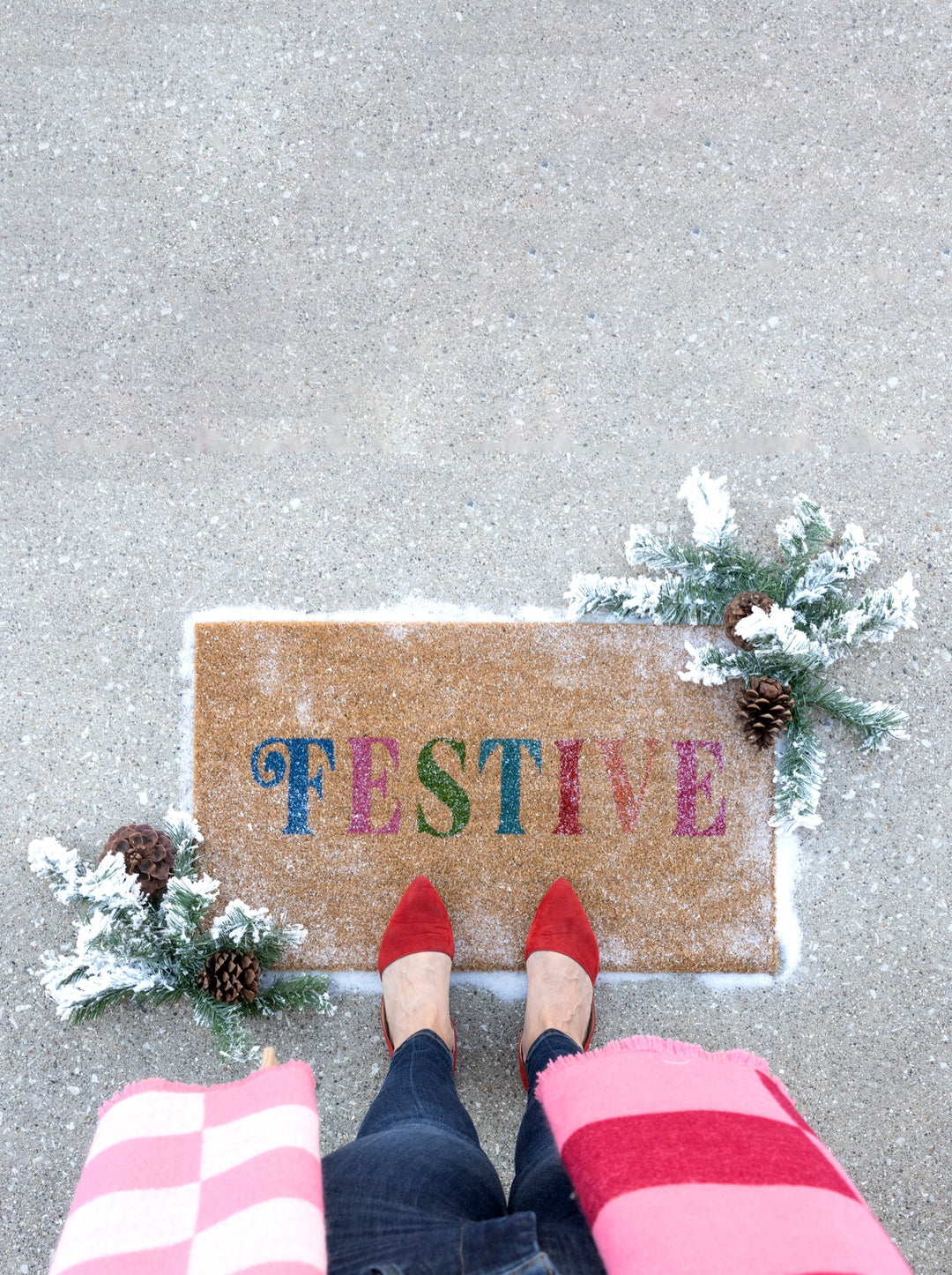 Festive doormat on a snowy porch with striped socks and greenery