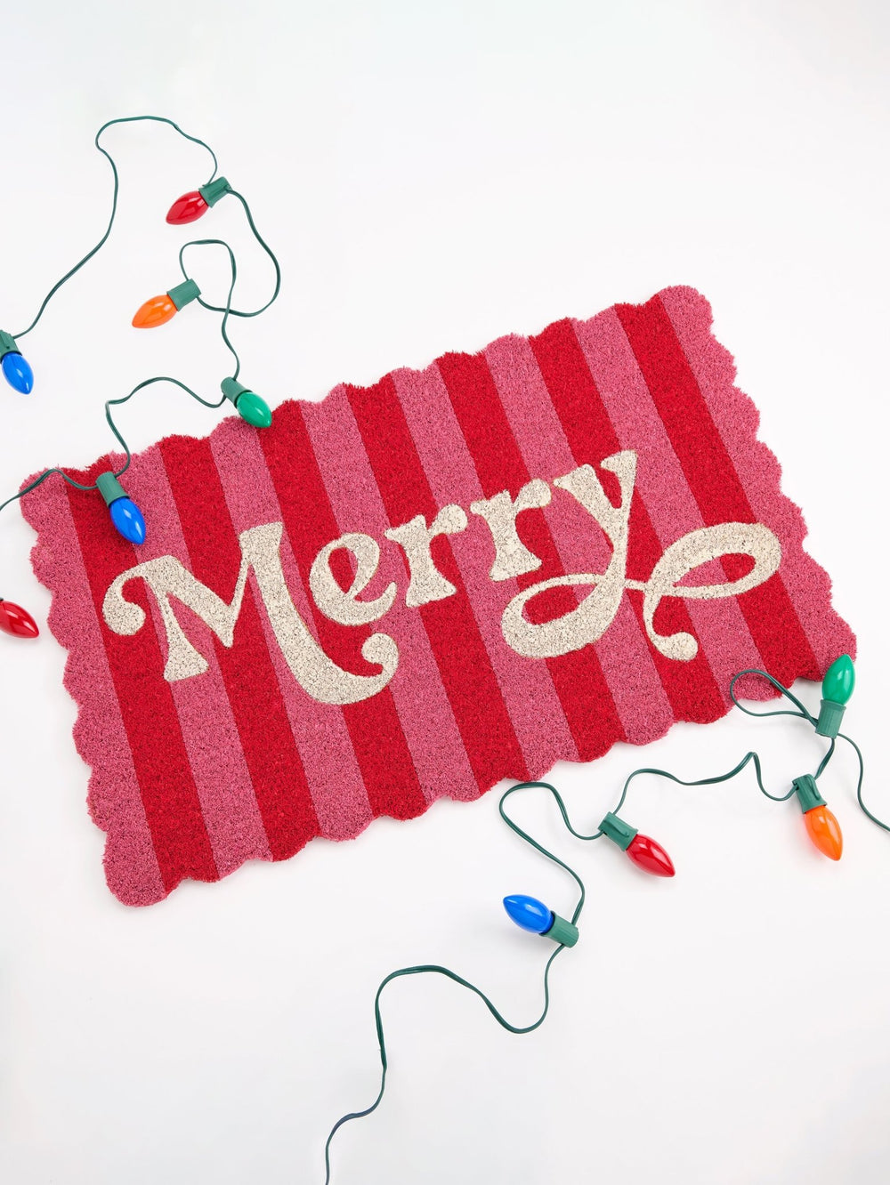 Pink Merry doormat styled on white with a strand of colorful vintage Christmas lights
