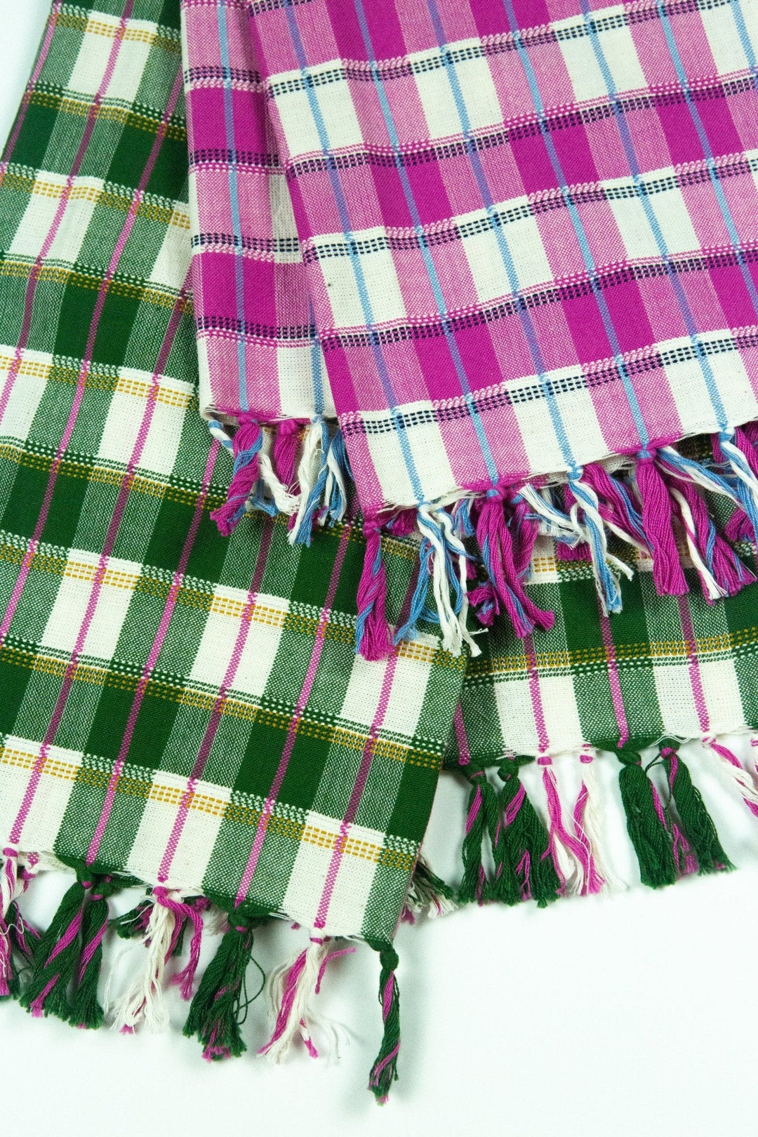Fringed ends of the forest green towel laid over a pink and white plaid towel