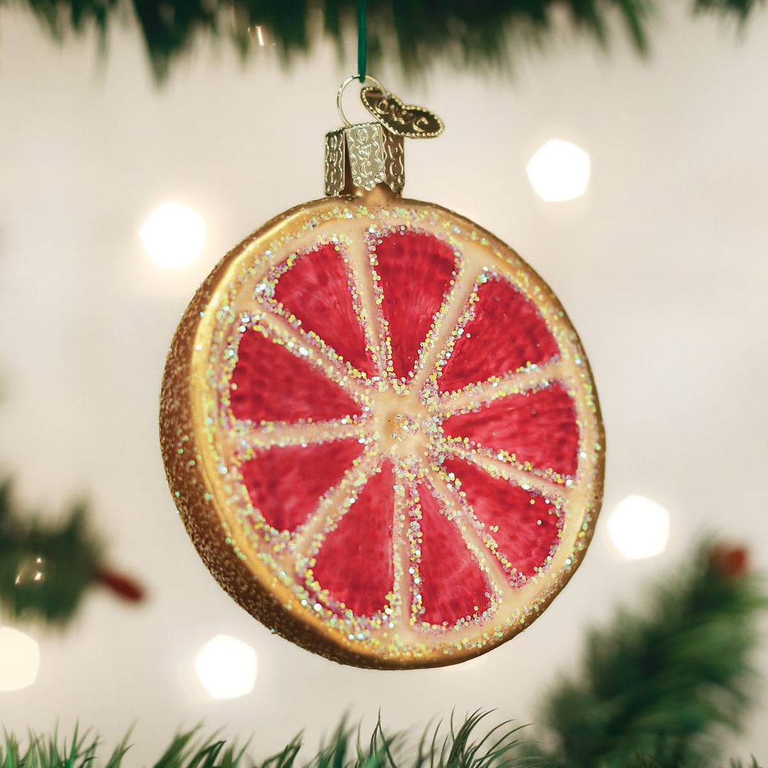 Pink grapefruit slice ornament hanging on a lit Christmas tree with warm bokeh lights