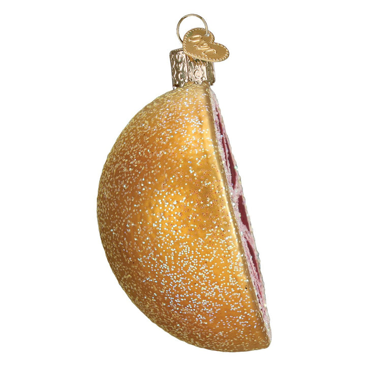 Side view of the grapefruit ornament showing the curved gold peel and pink cut edge, on white