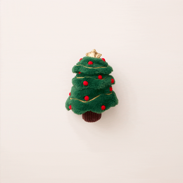 Green Christmas tree snuffle toy standing on its brown trunk against a pale pink background.