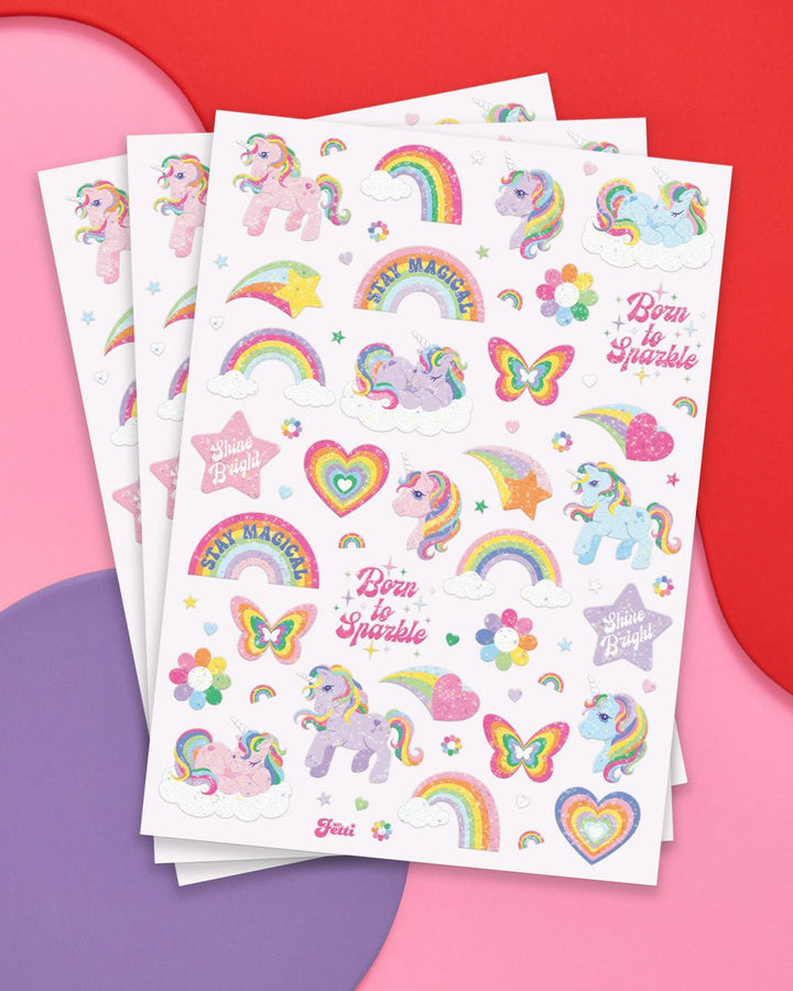 Three sheets of glitter unicorn temporary tattoos fanned on pink: unicorns, rainbows, butterflies, and Born to Sparkle