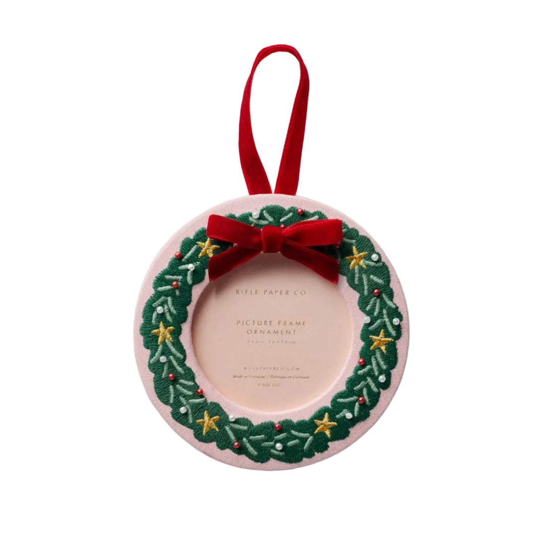 Round blush pink bookcloth photo frame ornament with embroidered green Christmas wreath, gold stars, and red velvet bow