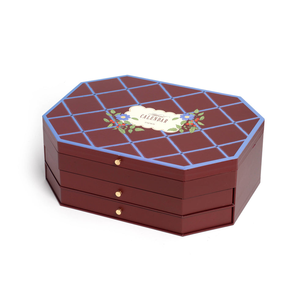 Closed burgundy advent calendar box with blue lattice lid and floral label, a luxury stationery gift for the holidays