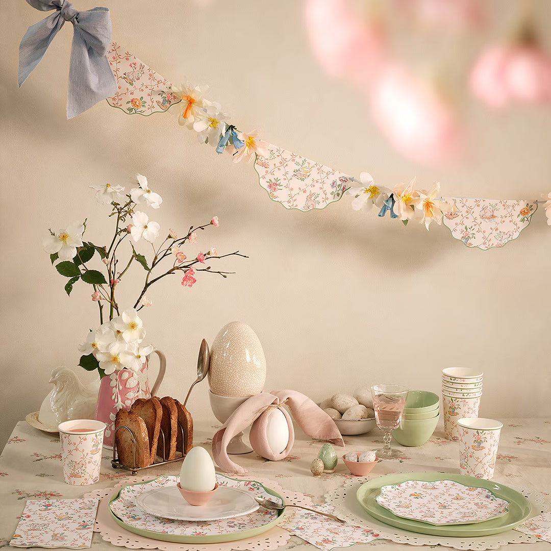 Vintage Garden Trellis garland with scalloped floral pennants, crepe paper flowers, and blue bows above an Easter table.
