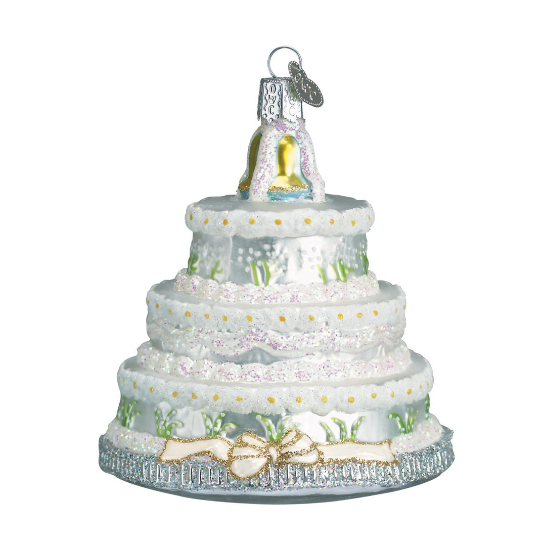 Front of the wedding cake ornament with white lace tiers, small flowers, and a gold bow, on white