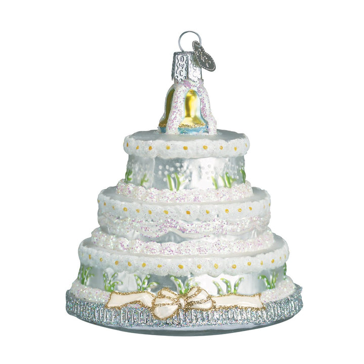 Front of the wedding cake ornament with white lace tiers, small flowers, and a gold bow, on white