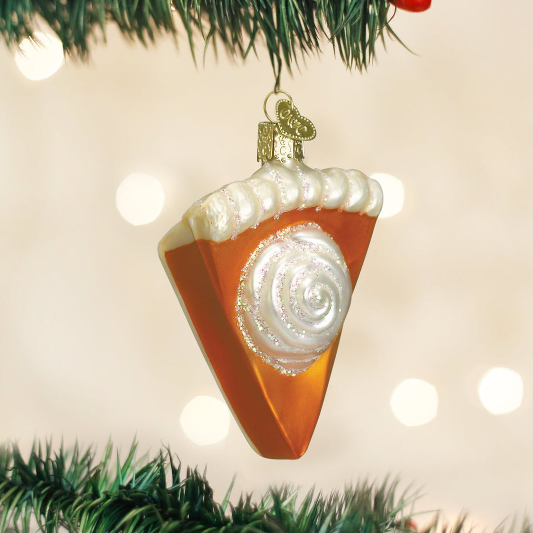 Pumpkin pie slice glass ornament hanging on a lit Christmas tree
