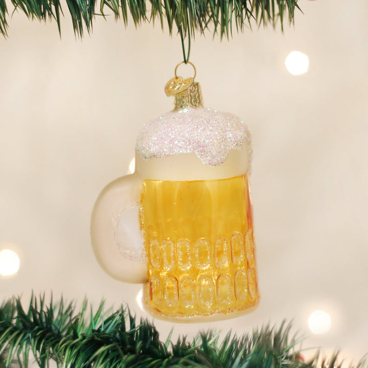 Beer mug ornament hanging on a Christmas tree with twinkle lights glowing behind it