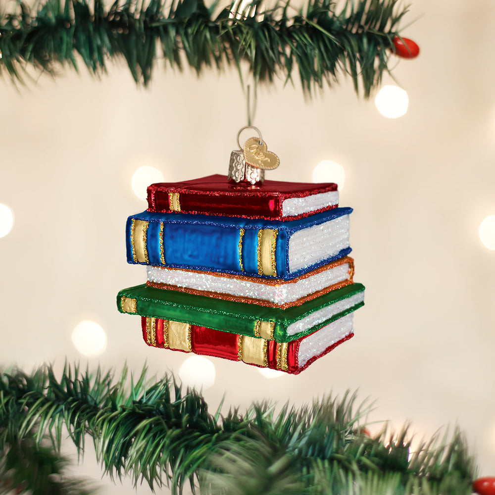 Stack of books glass ornament hanging on a Christmas tree branch with soft golden bokeh lights