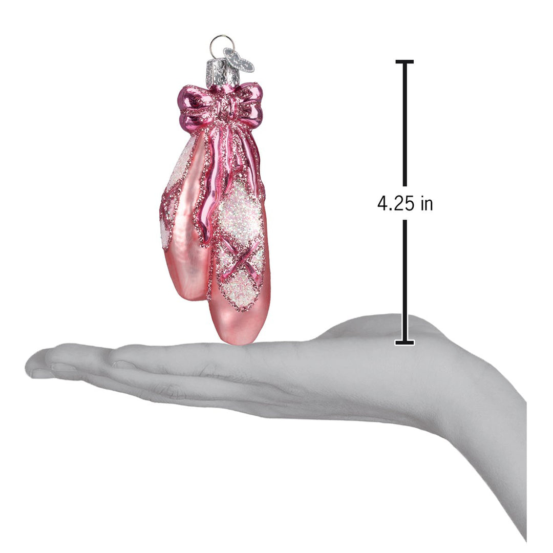 Pink ballet slippers ornament resting on an open hand with a 4.25 inch scale marker beside it