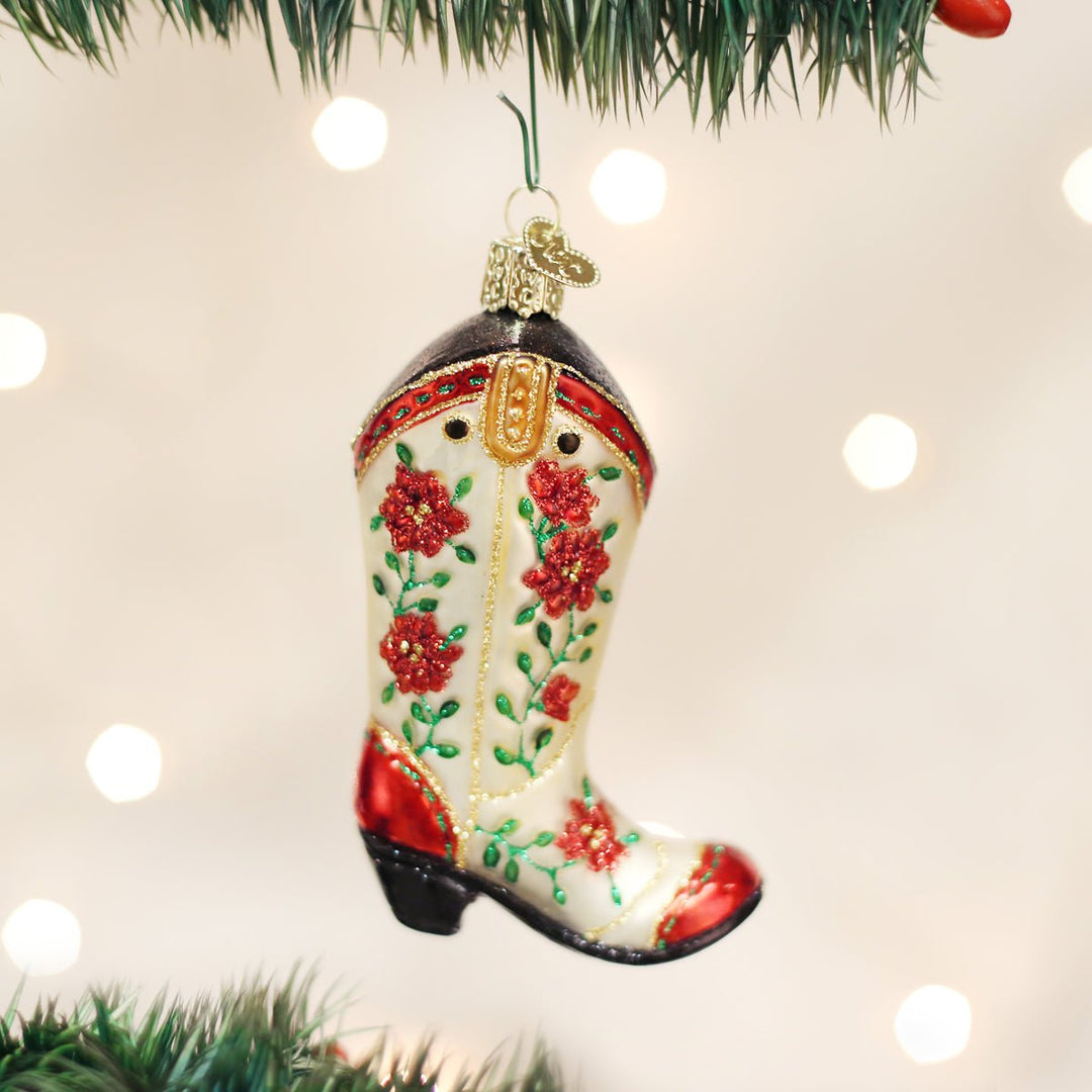 Poinsettia cowgirl boot ornament hanging on a lit Christmas tree with warm bokeh lights