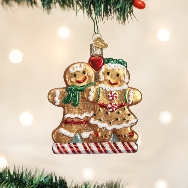 Two gingerbread cookie friends glass ornament hanging on a lit Christmas tree