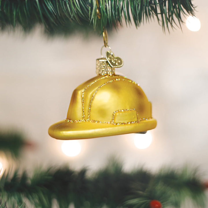 Construction hard hat ornament hanging on a lit Christmas tree with warm bokeh lights