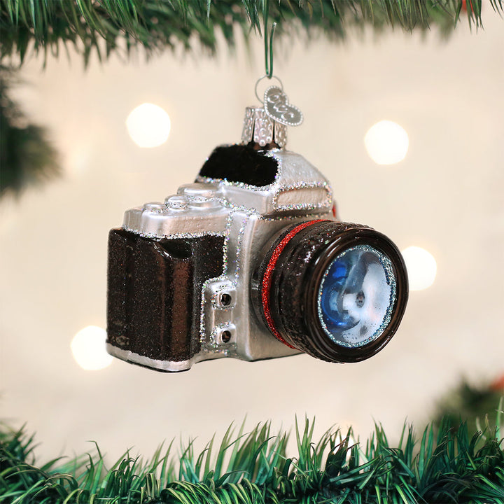 Camera Christmas ornament hanging on a tree branch with warm bokeh lights behind it