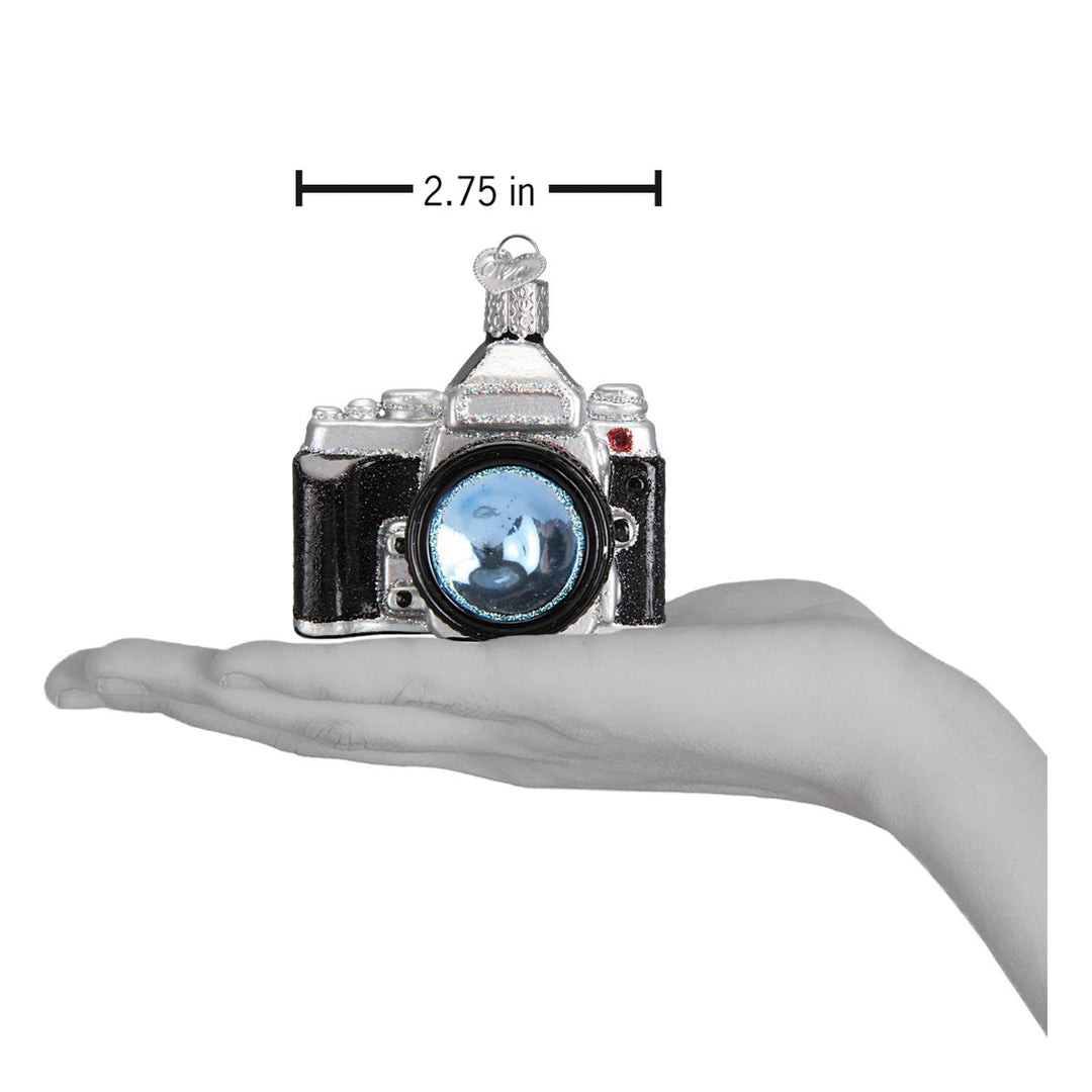 Camera ornament held above an open palm with a 2.75 inch width marker for scale