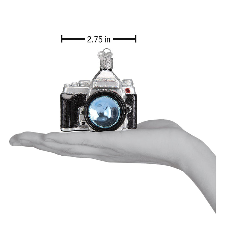 Camera ornament held above an open palm with a 2.75 inch width marker for scale