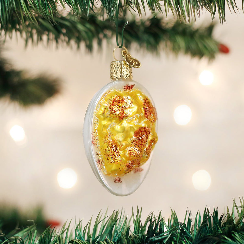 Deviled egg glass ornament with golden filling and paprika hanging on a Christmas tree branch