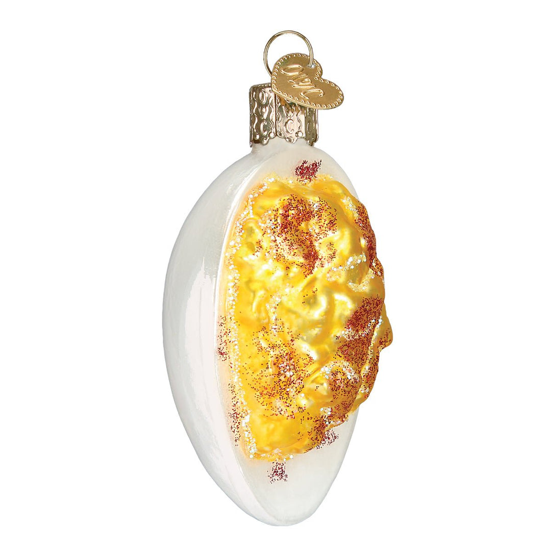 Side view of the deviled egg ornament showing the piped yellow filling and glittery paprika, on white