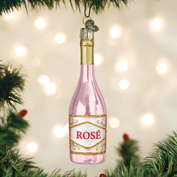 Pink rosé bottle ornament hanging on a Christmas tree with soft twinkle lights behind it