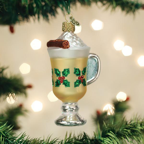 Eggnog mug glass ornament with holly, whipped cream, and a cinnamon stick hanging on a lit Christmas tree