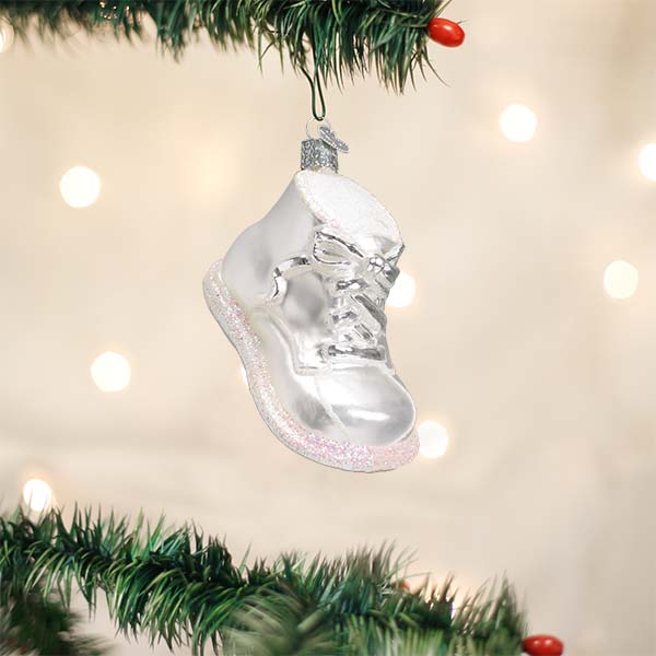 White baby shoe baby's first Christmas ornament hanging on a tree with warm bokeh lights