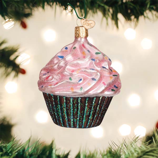 Pink frosted cupcake glass ornament hanging on a lit Christmas tree