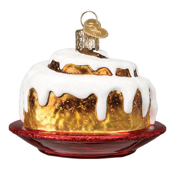 Cinnamon roll ornament with a golden swirl and dripping white icing on a red plate, front view on white