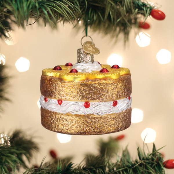 Pineapple upside down cake glass ornament hanging on a lit Christmas tree with soft bokeh lights