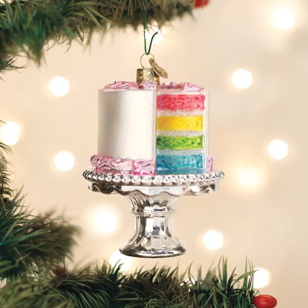 Rainbow layer cake glass ornament on a silver stand hanging on a lit Christmas tree